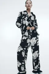 Pantalón de sarga suave con estampado floral en blanco y negro, tiro alto, cintura elástica con cordón ajustable, piernas rectas con puño en el bajo y detalle de doble línea blanca en el ruedo.