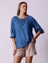 Blusa celeste de tencel con cuello a la base, escote en V con aplique de cordel y lazo de ajuste. Manga larga amplia con puño elastizado.