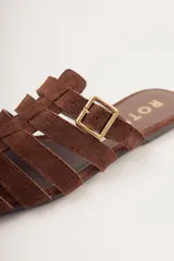 Sandalias planas de cuero color marrón con diseño de tiras entrecruzadas y hebilla lateral ajustable.