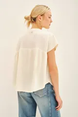 Camisa negra de manga corta con combinación de tejido de punto y plano, detalles de volados y frunces en pechera y espalda, acceso con botones fake nacar y medallita marcaria en espalda.