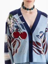 Cardigan oversize de punto jacquard multicolor con predominancia de celeste y azul marino. Cuenta con cuello en V, cierre frontal de botones y un diseño artístico que incluye bordados de cerezas y flores. Las mangas largas presentan un patrón de franjas horizontales.