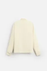 Camisa color crema de corte relaxed fit, confeccionada en tejido con mezcla de viscosa. Tiene cuello solapa, manga larga con puños abotonados, bolsillo de parche en el pecho y cierre frontal con botones.
