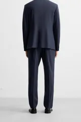 Pantalón de vestir azul marino, de corte slim fit, con bolsillos laterales y traseros de doble vivo con botón. Se ajusta a la cintura con cierre frontal con cremallera y botón.