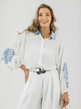 Camisa blanca de tela fresca con cuello camisero celeste y mangas abullonadas con apliques en denim celeste.