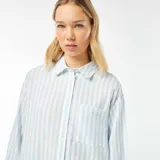 Camisa celeste y blanca a rayas verticales, de corte holgado, manga larga y bolsillo de parche en el pecho.