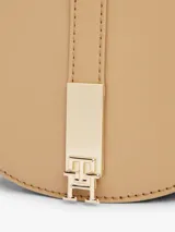 Cartera saddle color beige de poliuretano con correa extraíble ajustable, cierre de solapa magnético, dos compartimentos principales, compartimento con cremallera e insignia del monograma TH en la parte delantera.
