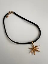 Gargantilla de cuero negro con dije dorado en forma de flor.