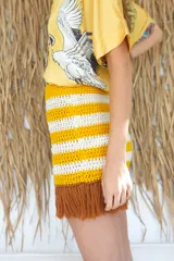 Minifalda tejida a mano en hilado de algodón, con diseño a rayas horizontales en color amarillo y blanco. Presenta flecos marrones en el ruedo.