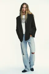 Blazer negro de corte oversize, con cuello solapa, escote pico, manga larga con hombreras y forro interior. Presenta bolsillos con solapa delanteros y bolsillo de vivo en el pecho.