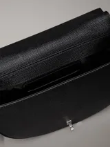 Cartera de hombro tipo saddle de Calvin Klein, color negro, con textura de lino tejido en piel sintética. Presenta correa ajustable, cierre de solapa con broche giratorio y herraje metálico con el monograma CK en la parte delantera.