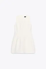 Vestido corto blanco de cuello redondo y sin mangas. Falda con pliegues y volumen. Cierre trasero con cremallera oculta.