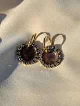 Par de aros colgantes con dije circular de resina con glitter multicolor y borde de strass. El arito es de acero quirúrgico dorado.