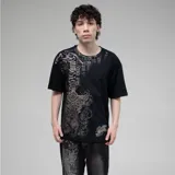 Remera negra de algodón con estampado frontal grande en tonos grises y dorados, con tipografía gótica, un diseño de cruz ornamentada y un felino en el centro.