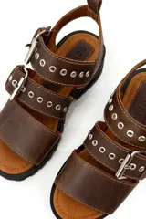 Sandalia de cuero color marrón chocolate, con dos tiras anchas sobre el empeine ajustables con hebillas metálicas plateadas.