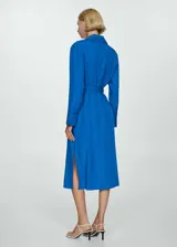 Vestido camisero midi color azul eléctrico, con cuello camisero, manga larga con puños abotonados, dos bolsillos de parche en el pecho, lazo ajustable en la cintura, cierre frontal con botones y aberturas laterales en el bajo.