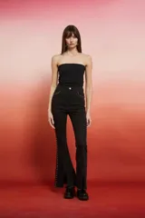 Pantalón jean negro de tiro alto, corte flare con tajo en el ruedo y detalles de tachas metálicas a los costados.