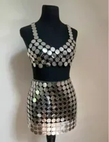 Conjunto plateado de top y falda corta, confeccionado con lentejuelas espejadas unidas por pequeñas argollas metálicas.