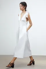 Vestido midi blanco de algodón, con escote pico pronunciado y tirantes anchos ajustables con lazada. Presenta elástico en la cintura y falda con pliegues.