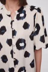 Blusa de manga corta con estampado de manchas negras y azules sobre fondo crema, cuello mao y cierre frontal con botones.
