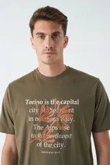 Remera verde militar de corte clásico con estampado frontal de texto en color ladrillo y dibujo de hojas.