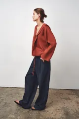 Blusa color ladrillo confeccionada en lino 100%. Tiene cuello fluido, mangas largas acampanadas y espalda descubierta ajustable con cordones.