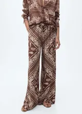 Pantalón de mujer de corte wide leg con estampado paisley en tonos marrones y beige. Tiene cintura elástica con lazo ajustable, tiro medio, dos bolsillos laterales y tejido ligero.
