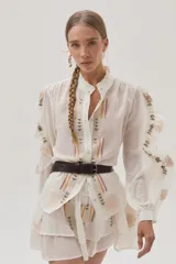 Blusa blanca de viscosa con cuello mao, cierre frontal con botones, mangas largas abullonadas con volados y bordados florales.