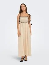 Vestido midi color crema, con tirantes finos ajustables, escote recto y cuerpo fruncido con detalle de borlas negras.