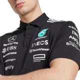 Polo oficial del equipo Mercedes-AMG Petronas Formula One Team, color negro, con cuello polo y botones frontales. Presenta detalles en blanco en los hombros y múltiples logos de patrocinadores en el pecho, incluyendo Mercedes-Benz, Petronas, INEOS, UBS, Crowdstrike, Snapdragon, TeamViewer, Hewlett Packard Enterprise y Signify.