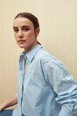 Camisa celeste de manga larga con cuello camisero y botones de nácar. Presenta detalles de broderie calado en el canesú y las mangas.