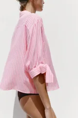 Camisa de lino a rayas verticales rosas y blancas, con cuello solapa, manga corta abullonada y lazos en los puños. Cierre frontal con botones ocultos.