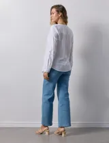 Camisa blanca de lino y rayón, con cuello a la base y escote en V abotonado. Tiene dos bolsillos con botón en el pecho y mangas largas regulables con presilla y botón.