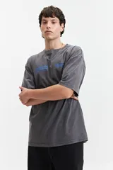 Remera gris de manga corta con corte oversize, cuello redondo y estampado con logos en el frente.