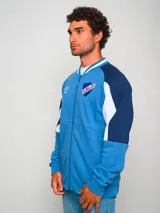 Campera bomber azul con mangas raglán en azul marino y detalles en blanco en cuello, puños y cintura. Presenta cierre frontal con cremallera, logo de Umbro bordado en el pecho y escudo del Club Nacional de Football.