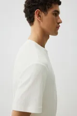 Remera blanca de punto texturizado de peso medio, corte estándar, cuello redondo y mangas cortas.