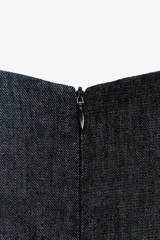 Vestido midi de denim azul oscuro, con cuello redondo y sisas. Presenta un aplique dorado en la cintura y abertura en la espalda. Cierre trasero con cremallera oculta.