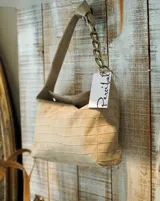 Cartera tipo bolso de mano color beige con textura símil piel de cocodrilo. Tiene correa corta de hombro con eslabones dorados.