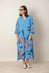 Vestido largo de lino color verde militar con estampado de hojas en tonos azul, naranja y marrón. Tiene cuello mao con botones, mangas tres cuartos y un bolsillo en el pecho.
