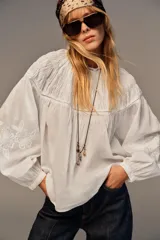 Camisa blanca de cuello redondo con detalle de nido de abeja y entredoses. Manga larga con bordados a tono y cierre trasero con botones.