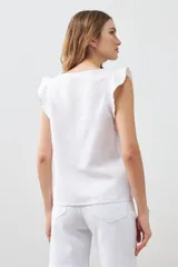 Blusa blanca sin mangas de lino con cuello redondo y volados en los hombros.