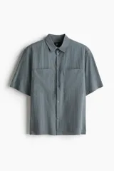 Camisa de manga corta color gris con dos bolsillos frontales con solapa y cierre de botones.