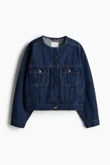 Campera de denim azul oscuro de algodón grueso con cuello redondo y solapa rompevientos guateada con botones ocultos. Modelo de corte holgado con hombros apenas caídos y puños ceñidos con botón. Bolsillos superiores con solapa y botón, bolsillos laterales discretos y trabillas ajustables con botón en el bajo.