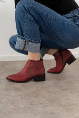 Bota corta color bordó de cuero vacuno, con puntera fina y detalle de textura escamada en el empeine. Tiene cierre lateral y taco cuadrado.