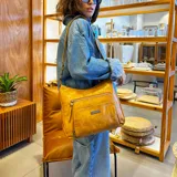 Bandolera marrón de símil cuero con correa larga regulable. Tiene dos bolsillos frontales con cierre, apertura superior con cierre, bolsillos internos con cierre y abiertos, y un bolsillo trasero con cierre.