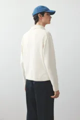 Remera polo de punto fino color crema, de manga larga con puños y bajo acanalados.