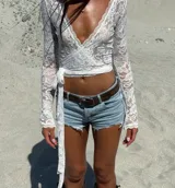 Blusa blanca de encaje con escote en V cruzado, mangas largas y lazo lateral.