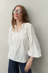 Blusa blanca de algodón con encaje floral en la parte superior, mangas largas abullonadas y escote con lazo.