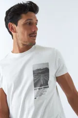 Remera blanca de algodón con cuello redondo y estampado rectangular con imagen de una carretera y texto en el frente.