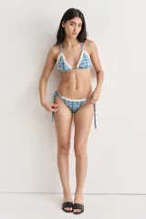 Conjunto de bikini celeste con estampado de flores y puntilla de algodón blanca en crochet. El corpiño es de corte triangular y la bombacha es regulable con lazos laterales.