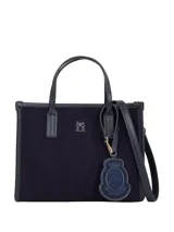 Cartera tipo tote bag de estructura rígida, color azul marino, con cuerpo principal de material textil tipo fieltro y ribetes y asas de poliuretano liso. Presenta un pequeño logo metálico TH en la parte frontal superior y un colgante decorativo con el escudo de la marca.